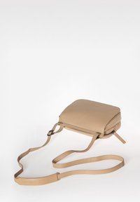 Borsa a tracolla in pelle beige con forma quadrata, chiusura con zip, tracolla regolabile e texture liscia. Design minimalista senza pattern.