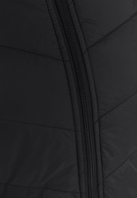 Tissu de veste matelassée noire avec une fermeture éclair verticale. La surface présente des lignes matelassées et une texture lisse, soulignant l'isolation.