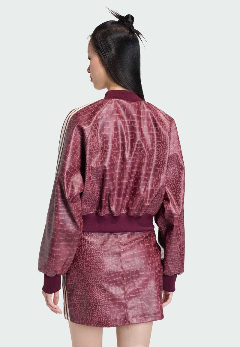 Veste bomber bordeaux à motif crocodile avec col et poignets côtelés, assortie d'une jupe fitted. Présente des rayures blanches sur les côtés.