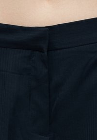 Μαύρη ζώνη παντελονιού με φερμουάρ, φορεμένη από άτομο με ανοιχτόχρωμη επιδερμίδα ορατή πάνω από τη ζώνη.