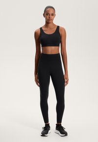 Črn športni kratki top in legice z visokim pasom. Gladek, raztegljiv material z diskretnimi šivi. Nosi se z črnimi tekaškimi čevlji.