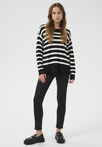 Sweter w czarno-białe paski o luźnym kroju z ściągaczami, w komplecie z czarnymi dopasowanymi dżinsami i czarnymi loafersami.