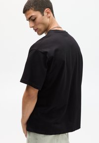 T-shirt nera in cotone con maniche corte, scollatura rotonda e vestibilità rilassata. Texture liscia senza motivi o decorazioni visibili.