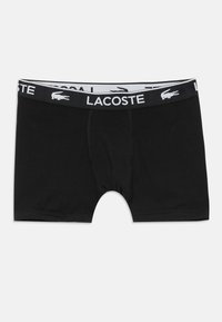 Boxer briefs neri realizzati in materiale morbido, con una cintura elastica bianca che presenta la scritta "LACOSTE" e un logo a forma di coccodrillo.