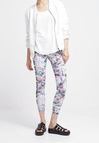 Vícebarevné legíny s květinovým vzorem, bílé tričko na ramínka a bílá bomber bunda. Černé platformové sandály dokončují celý outfit.
