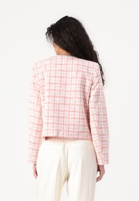 Rosa rutete tweedjakke med en kort design, lange armer og en teksturert finish. Kombinert med hvite stripete bukser.