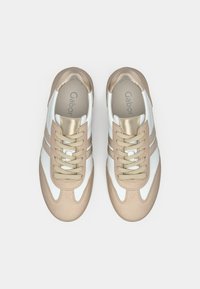 Αθλητικά παπούτσια με λευκό δερμάτινο πάνω μέρος, μπεζ σουέτ λεπτομέρειες, μπεζ κορδόνια και μεταλλική χρυσή γλώσσα. Διαθέτουν τρεις μπεζ ρίγες στα πλευρά.