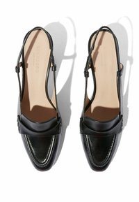 Zapatos slingback de cuero negro con punta redonda, que presentan un acabado suave, diseño de empeine plegado y una delgada correa ajustable en el tobillo.