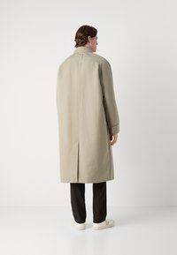Lichtbeige overjas gemaakt van een gladde, waterbestendige stof. Beschikt over een ventilatieopening aan de achterkant en minimalistische ontwerpelementen.