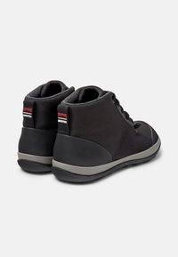 Zapatos de caña alta negros hechos de tela texturizada con una suela de goma gris. Presentan etiquetas rojas en la parte trasera y cordones para un cierre seguro.