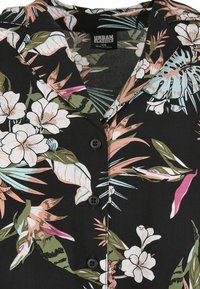 Black floral short-sleeve shirt featuring white flowers, green leaves, and pink accents. Button closure and soft fabric. Brand label visible.