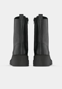 Μαύρες δερμάτινες μποτες μέχρι τον αστράγαλο με λείο φινίρισμα, χαρακτηριστικά χοντρή σόλα, πλαϊνούς φερμουάρ και λαβές για εύκολη χρήση.