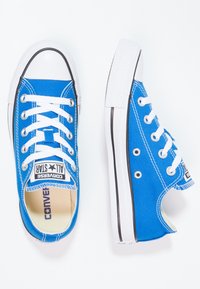 Blå kanvas låga sneakers med vita snören, gummikåpa vid tån och sidöglor. Har svart trim längs sulan och märkning på tungan.