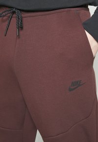 Bordeaux nike tepláky s černým logem, elastickým pasem na šňůrku a hladkým povrchem s detailním panely.
