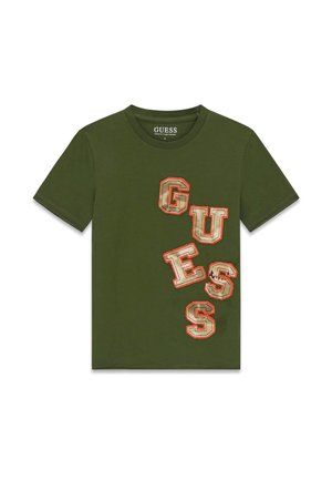 T-shirt à manches courtes vert olive avec de grandes lettres beiges et orange en contour formant le mot « GUESS » en diagonale sur le devant.