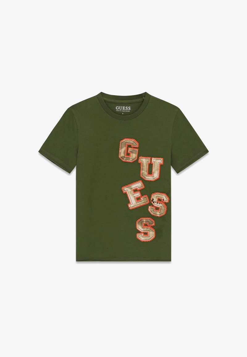 T-shirt à manches courtes vert olive avec de grandes lettres beiges et orange en contour formant le mot « GUESS » en diagonale sur le devant.