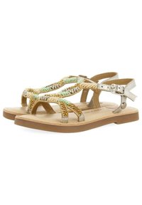 Sandalias planas trenzadas con acentos en dorado, verde y beige. Cuentan con una hebilla metálica plateada y una suela cómoda en tono marrón. Diseño abierto para una mejor transpirabilidad.