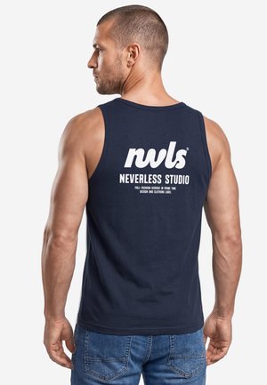 Man with short hair wearing a navy blue sleeveless shirt with white text "nwls Neverless Studio" on the back, paired with blue jeans.