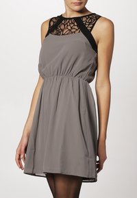 Graues ärmelloses Kleid mit taillierter Passform, das über ein schwarzes Spitzen-Mieder und schwarze Träger verfügt. Der Stoff wirkt glatt mit einem sanften Fall.