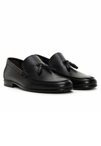Black leather loafers featuring textured uppers, smooth edges, decorative ties, and a low stacked heel. Rounded toe design.