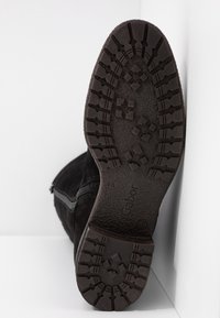 Botte en suède noire avec une semelle en caoutchouc texturée présentant un motif à relief. Fermeture éclair sur le côté et logo embossé sur la semelle.