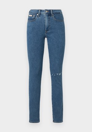 Vaqueros de mezclilla azul deslavada con un ajuste slim, que incluyen un detalle rasgado en la rodilla derecha y un diseño clásico de cinco bolsillos.