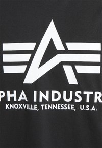 Černé bavlněné tričko s bílým logem s trojúhelníkovými a pruhovanými vzory a textem "ALPHA INDUSTRY KNOXVILLE, TENNESSEE, U.S.A."