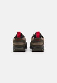 Zapatillas deportivas en color marrón y negro con una superficie texturizada, tiradores rojos y suelas de goma. Presentan el logotipo de la marca en el talón.