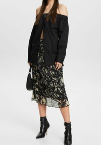 Camisa negra sin hombros, abotonada, combinada con una falda maxi de estampado negro y beige. Botines negros con punta afilada y detalle de cremallera.