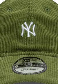 Grüne Corduroy-Baseballmütze mit einem weißen gestickten "NY"-Logo auf der Vorderseite und einem runden verstellbaren Etikett unter dem Schirm.