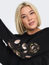 Mustast särkveluurist pikkade varrukatega pusa, mille varrukatel on kuldse, roosakuldse ja musta metallilise lilleline litrite tikand. Pehme kangapositsioon.