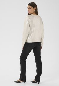 Maglione metallico argento a maglia con maniche lunghe, polsini e orlo a coste; abbinato a jeans neri a gamba dritta e ballerine nere a punta.