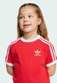 Red cotton t-shirt with white collar and sleeves, featuring three white stripes on shoulders and an embroidered adidas logo on the chest.