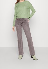 Hellgrüner, gerippter Pullover, graue, hochtaillierte Jeans und glänzende grüne Stiefeletten mit quadratischen Absätzen. Einfaches, zeitgemäßes Design.