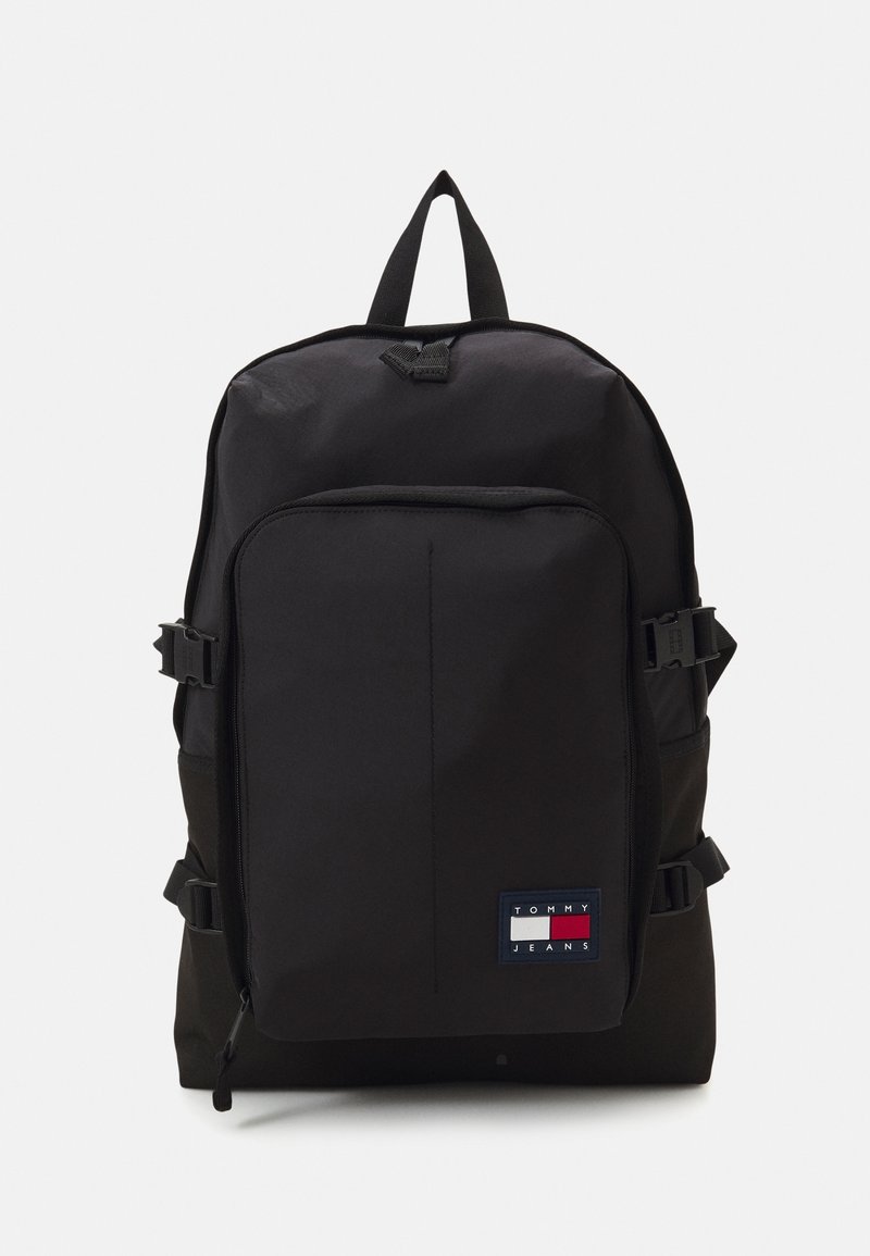 Sac à dos noir avec poche avant zippée et écusson logo Tommy Jeans en bas à droite, avec des sangles latérales à boucle et une poignée supérieure.