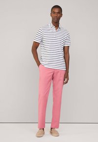 Gestreiftes Poloshirt in Weiß und Marineblau, kombiniert mit rosa Hose. Das Shirt hat einen Kragen und kurze Ärmel; die Schuhe sind braune Slipper.