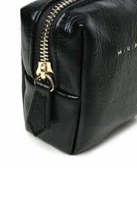 Borsa cosmetica nera in pelle sintetica con forma rettangolare, cerniera dorata e dettagliato con etichetta. Presenta una superficie texture con cuciture visibili.