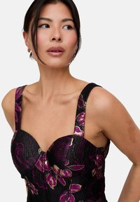 Schwarzes Korsett-Top mit lila Blumenmuster, ausgestattet mit breiten Trägern, einem strukturierten Oberteil und metallischen goldfarbenen Akzenten. Die strukturierte Stoffoberfläche verleiht Tiefe.