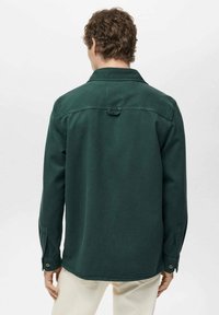 Camicia verde a maniche lunghe con colletto, dettaglio sulla spalla posteriore e polsini con bottoni, realizzata in un tessuto testurizzato. Visualizzata da dietro.