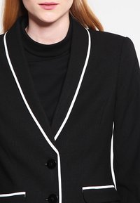 Svart kavaj med vit piping, dubbelknappning, slitna slag, strukturerad passform och subtilt texturerat tyg.