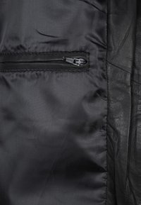Gros plan sur un tissu noir avec une petite poche fermée par une fermeture éclair et un matériau en cuir noir texturé adjacent.