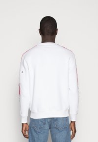 Felpa bianca con strisce rosse sui lati, polsini e orlo a costine. Presenta una tasca inclinata sul maniche sinistro. Design casual con una vestibilità rilassata.