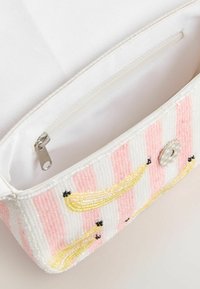 Pochette blanche avec des rayures verticales roses et des motifs de bananes perlées jaunes, dotée d'une fermeture magnétique argentée et d'une poche intérieure zippée.