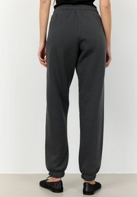 Grå sweatpants av mjukt tyg med elastisk midja och åtsittande muddar vid anklarna. Bärs med svarta vävda skor.