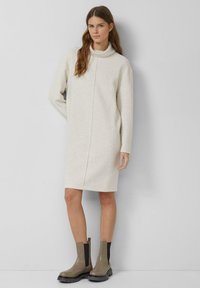 Jasnobeżowa sukienka z długim rękawem i wysokim kołnierzem, z centralnym szwem. Połączona z taupe kozakami za kolano z czarnymi akcentami.