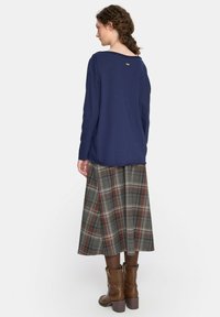 Granatowa bluzka z długim rękawem ozdobiona szczegółami na plecach, zestawiona z spódnicą w kratkę do kolan w ziemistych odcieniach oraz brązowymi botkami za kostkę.