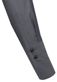 Grå skjortsärm med en slät textur, prydd med två svarta knappar och en skräddarsydd manschettdesign. En subtil sömnadsdetalj är synlig.