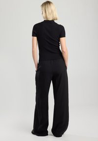 Black ribbed knit top with short sleeves paired with black wide-leg pants. Smooth texture and relaxed fit. Simple design with no visible patterns.