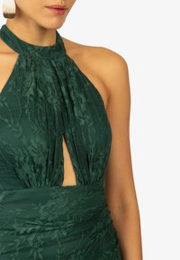 Groene kanten halterjurk met een keyhole-ontwerp, textuurstof en bloemenpatronen. De tailleband verzamelt voor een aansluitende silhoutte.