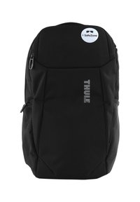Un sac à dos noir avec une finition texturée, présentant un logo THULE bien en vue. Comprend une étiquette SafeZone circulaire et des poches zippées.